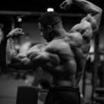 Black and white photo of a bodybuilder flexing muscles indoors.